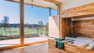 Un dormitorio moderno con cama de madera, un amplio ventanal corredero que da a un balcón y vistas a un campo verde.