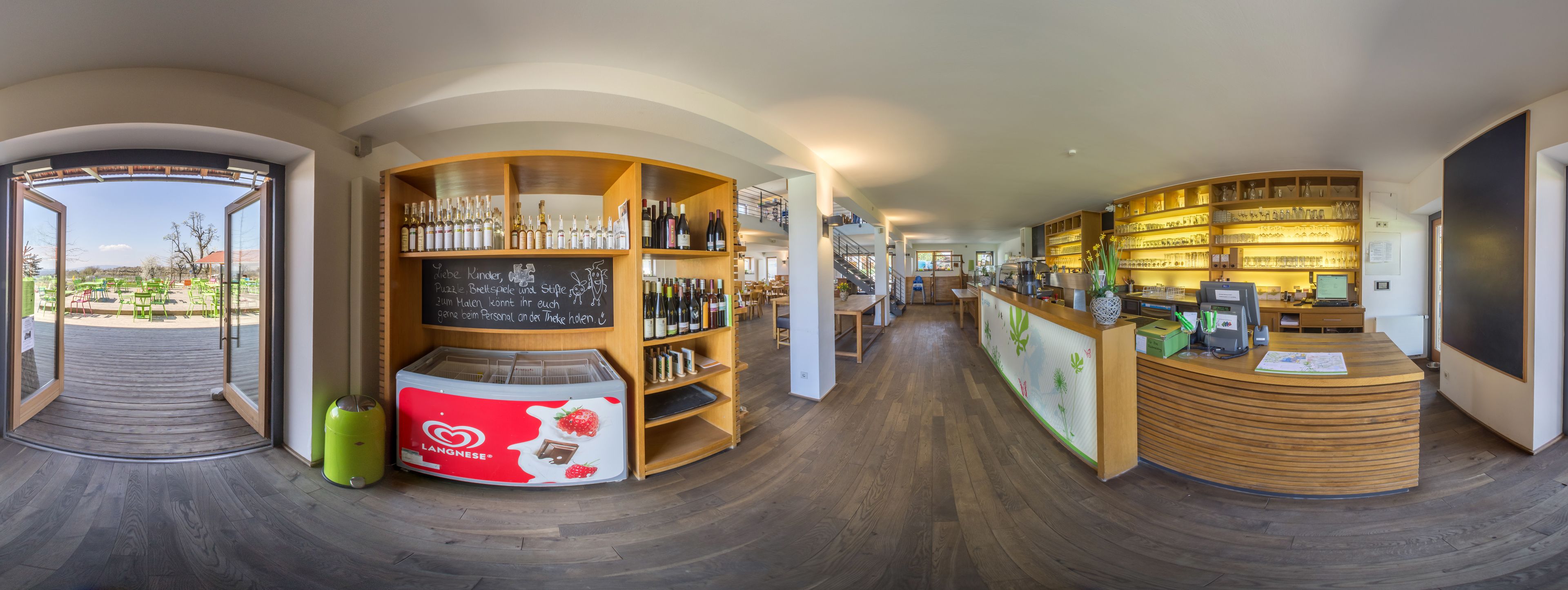 A modern bar area with wooden shelves displaying bottles, a chalkboard menu, and a reception desk.