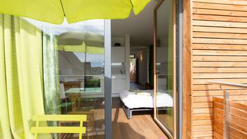 A modern room with a bed, a glass door leading to a balcony, and a small kitchenette.