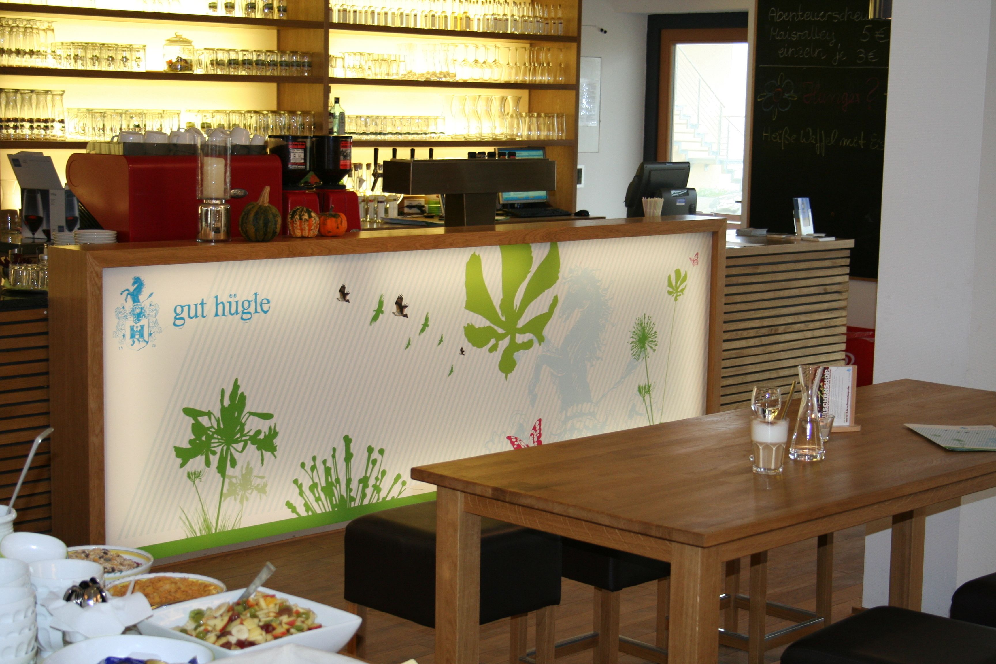 A restaurant interior with a wooden counter, a menu board, and a wall with green plant decals.