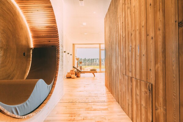 A modern interior with a curved wooden wall, a wooden floor, and a seating area with a bench and cushions. - Gut Hügle Erlebnishof (Ravensburg)