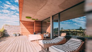 Eine moderne Außenterrasse mit Holzboden, Lounge-Stühlen und einer Glaswand mit Blick auf die Landschaft.