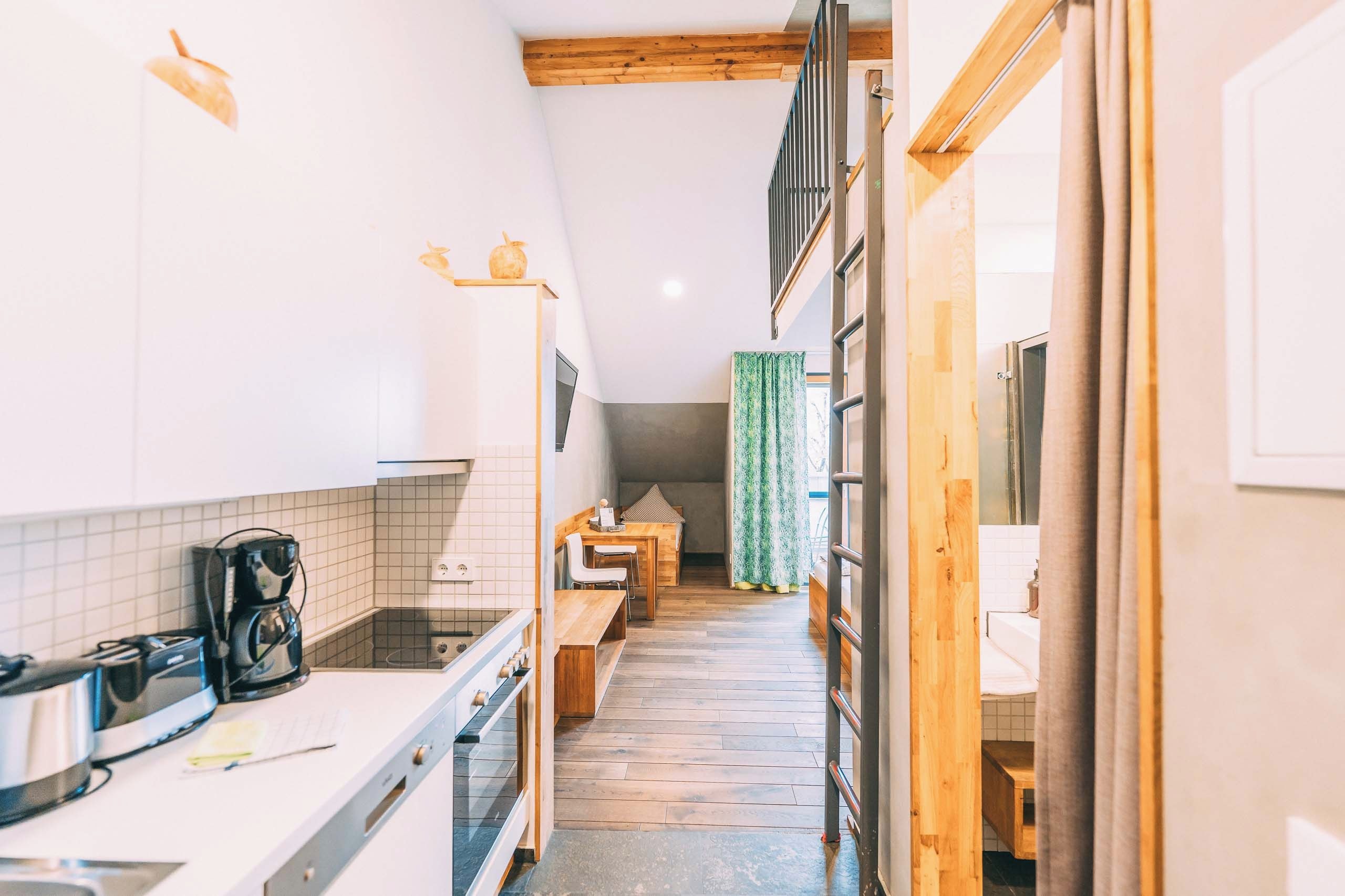 A narrow kitchen with a coffee machine, a dining area with a table and chairs, and a view into a bathroom with a shower.