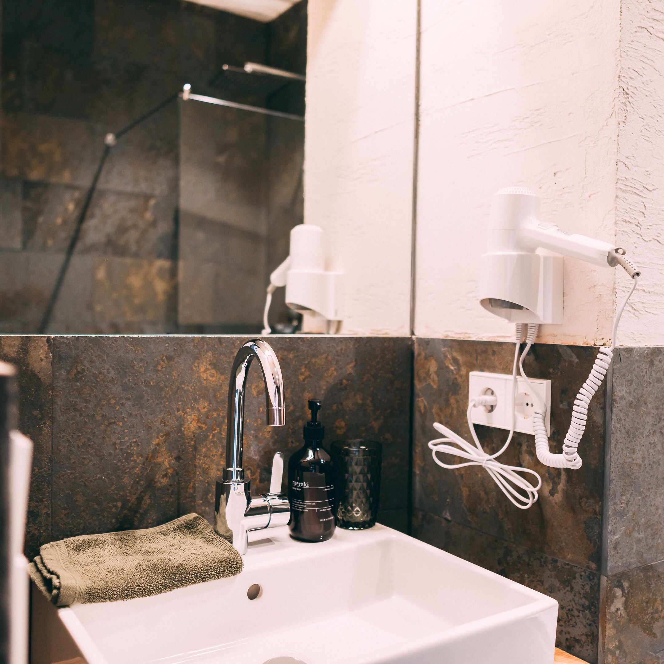 A bathroom with a white sink, a mirror, a towel, and a hairdryer mounted on the wall.