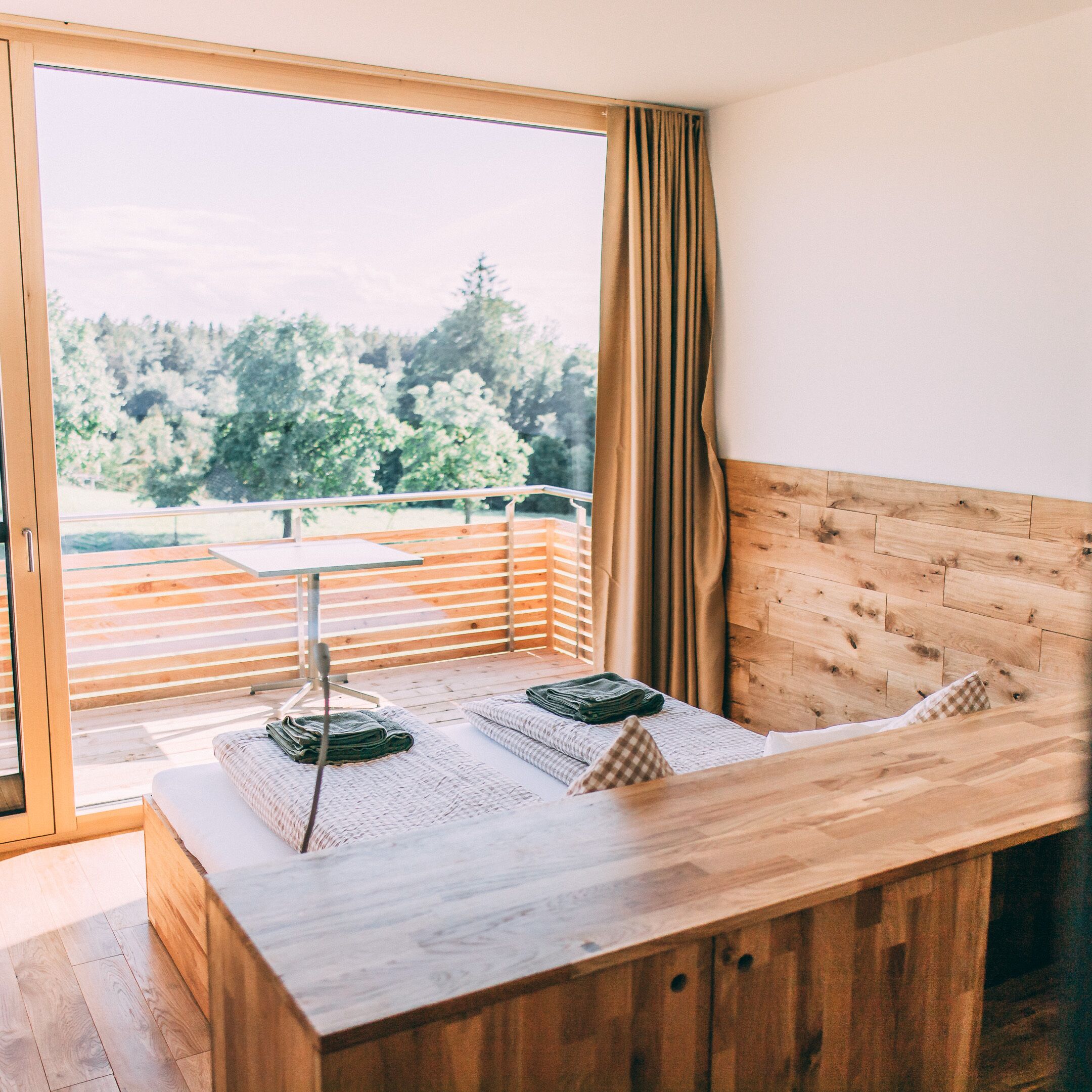A room with a wooden bench, a table, and a view of trees through a window.