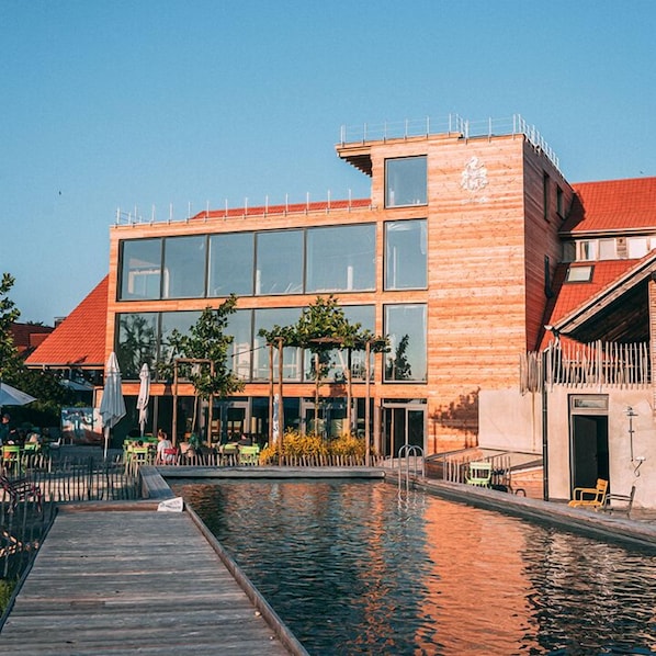 A modern building with large windows and a wooden facade, adjacent to a calm water body with a wooden dock. - Gut Hügle Erlebnishof (Ravensburg)