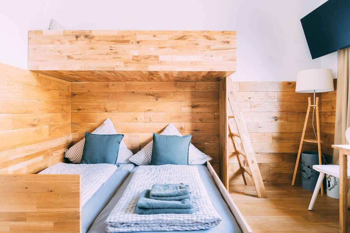 Una habitación acogedora con cabecera de madera, cama con ropa de cama azul y blanca y un escritorio con lámpara.