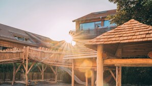 Eine hölzerne Spielkonstruktion mit Rutsche und Kletterelementen neben einem Gebäude mit Balkon.