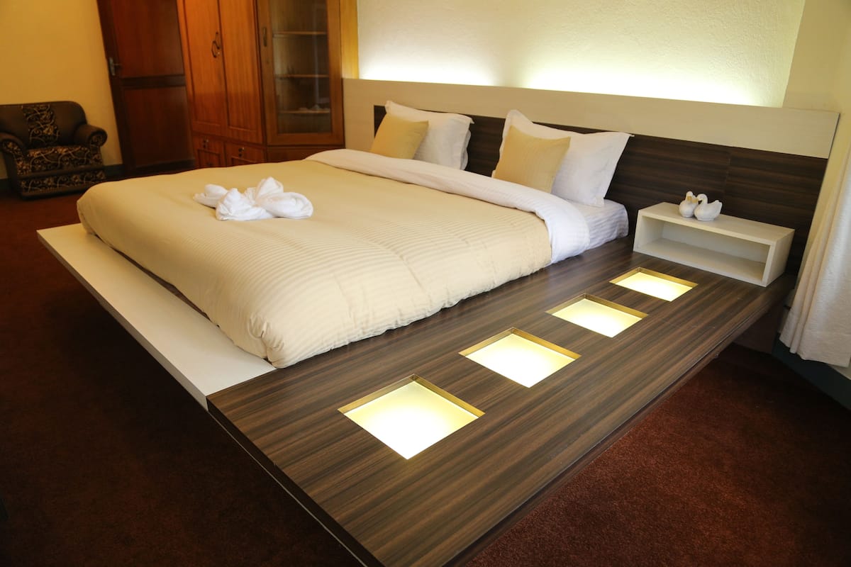A modern hotel room with a large bed, bedside tables, and a wardrobe.