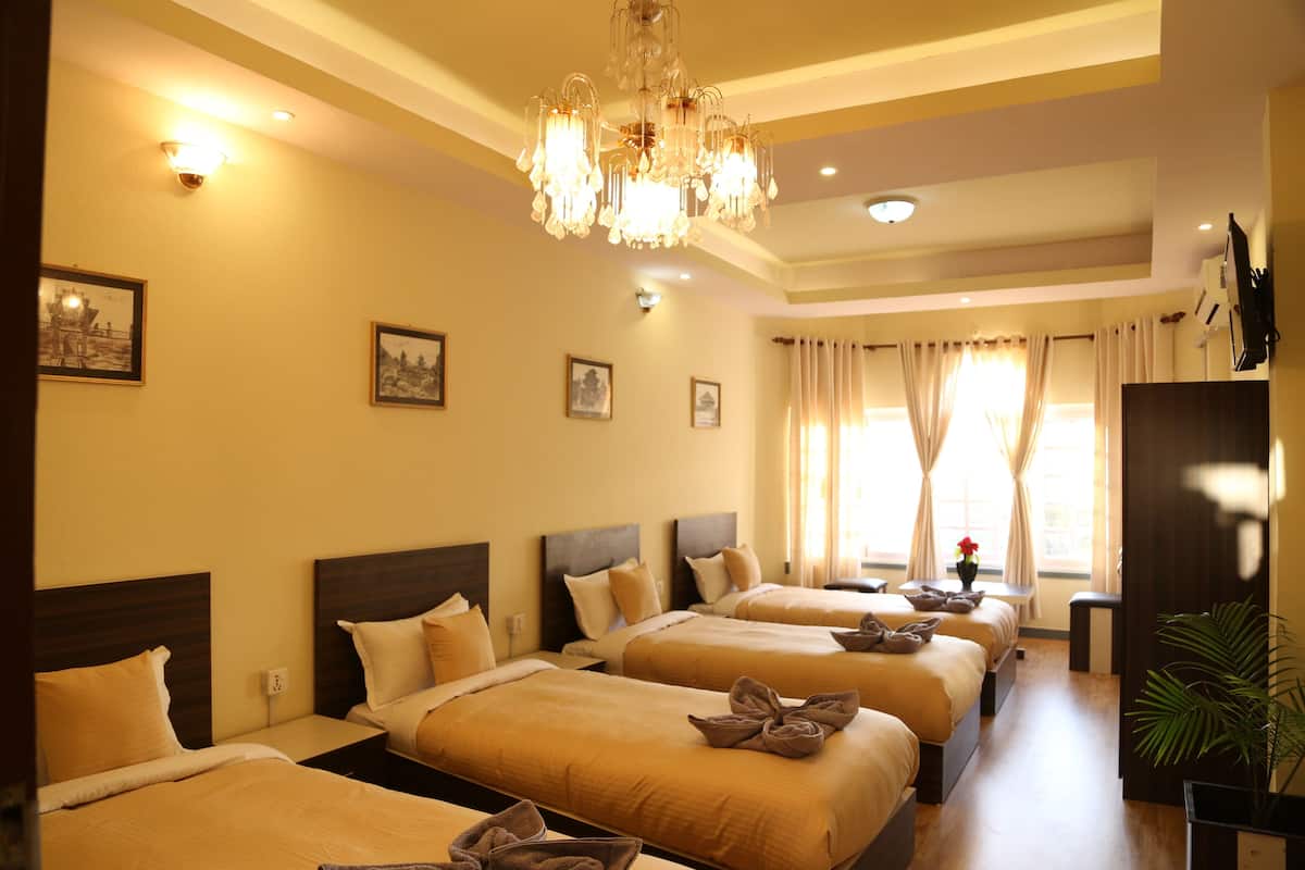 A hotel room with three beds, a chandelier, framed pictures on the wall, and a television on the wall.