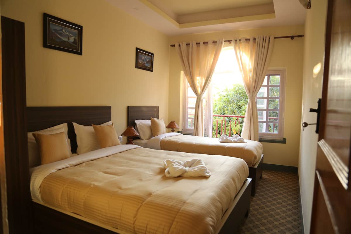 A hotel room with two beds, a window with curtains, and a door.