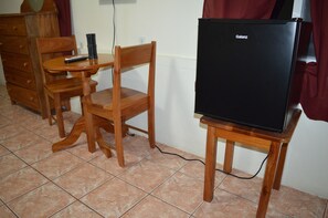 A small room with a wooden table, a wooden chair, a black Galanz refrigerator, and a wooden dresser.