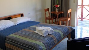 A hotel room with a bed, a small table with a vase of flowers, two chairs, and a television. - Sugar Patch Inn (Hopkins)