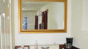 A bathroom with a wooden vanity, a mirror with a gold frame, a sink, a coffee maker, and a trash bin. - Sugar Patch Inn (Hopkins)