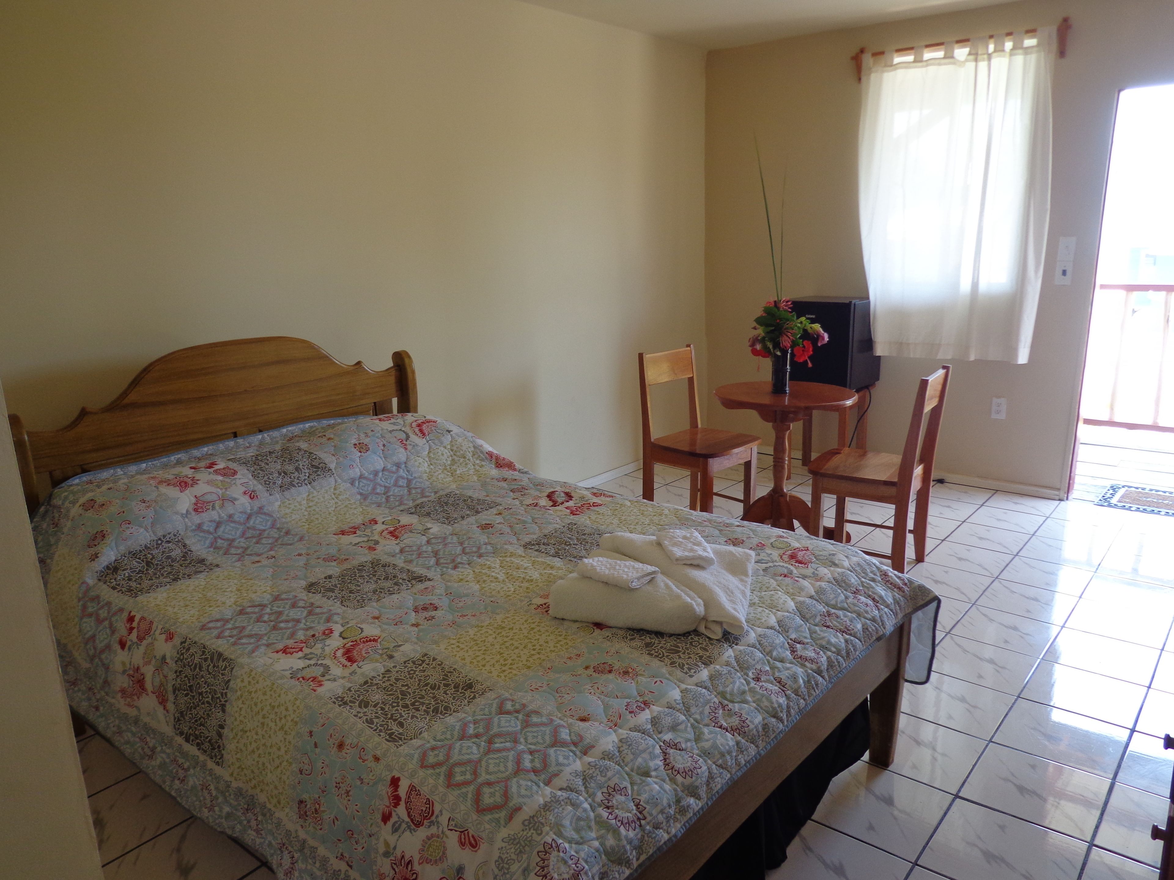 Una cama bien tendida con un edredón floral, un cabecero de madera y una mesita con un florero.