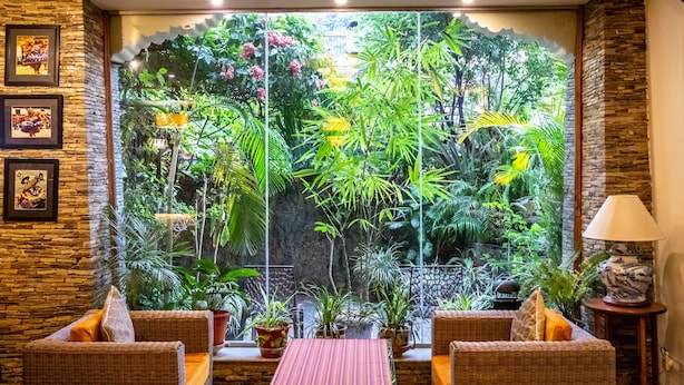 Habitación con mobiliario de mimbre, una pequeña mesa y vistas a un jardín exuberante a través de un muro de cristal.