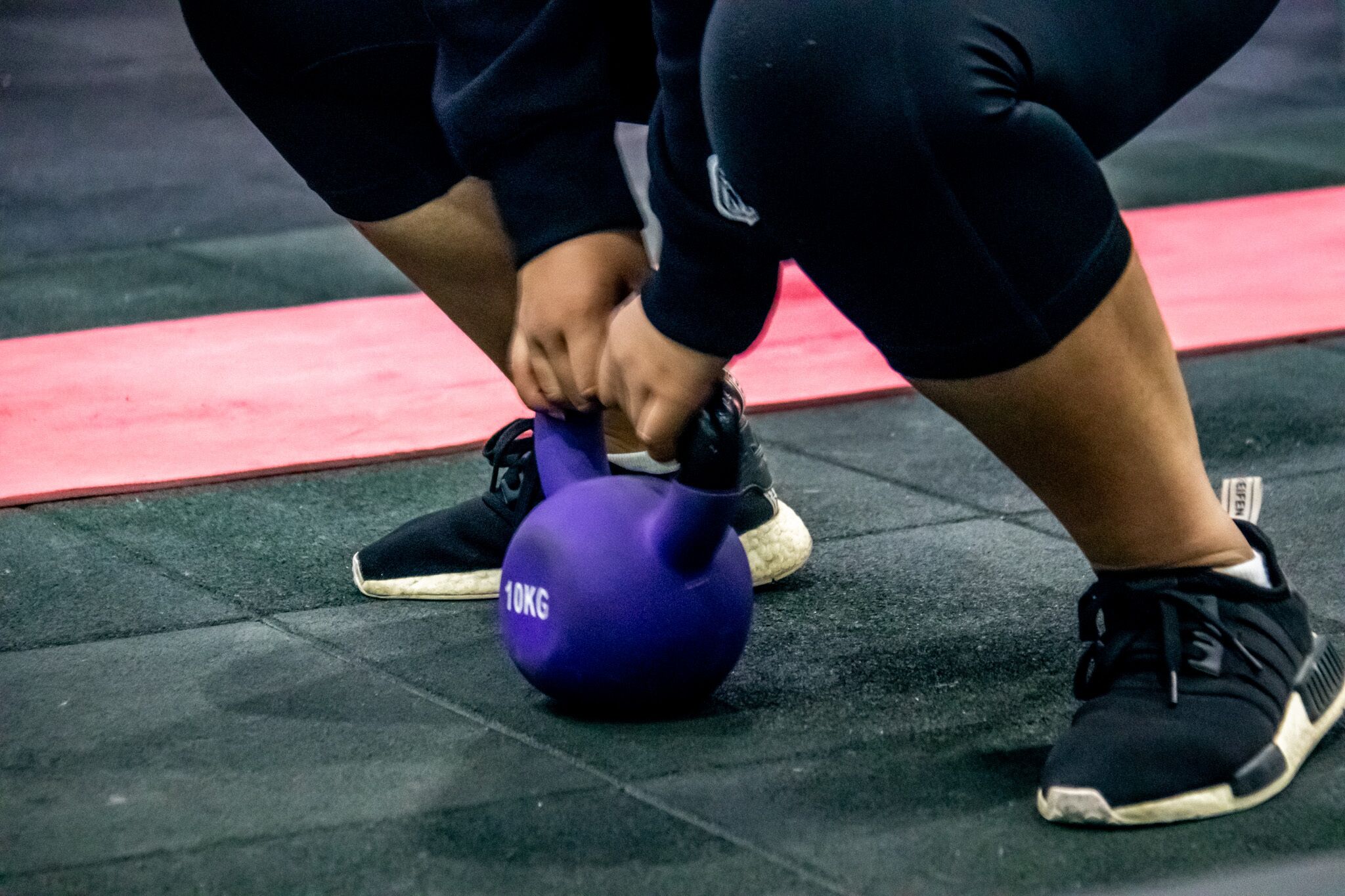 A person performing a kettlebell exercise on a rubber mat with a red border.