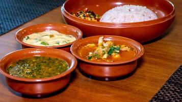 Una mesa de madera con cuatro cuencos que contienen diferentes platos, incluyendo arroz y una salsa verde.