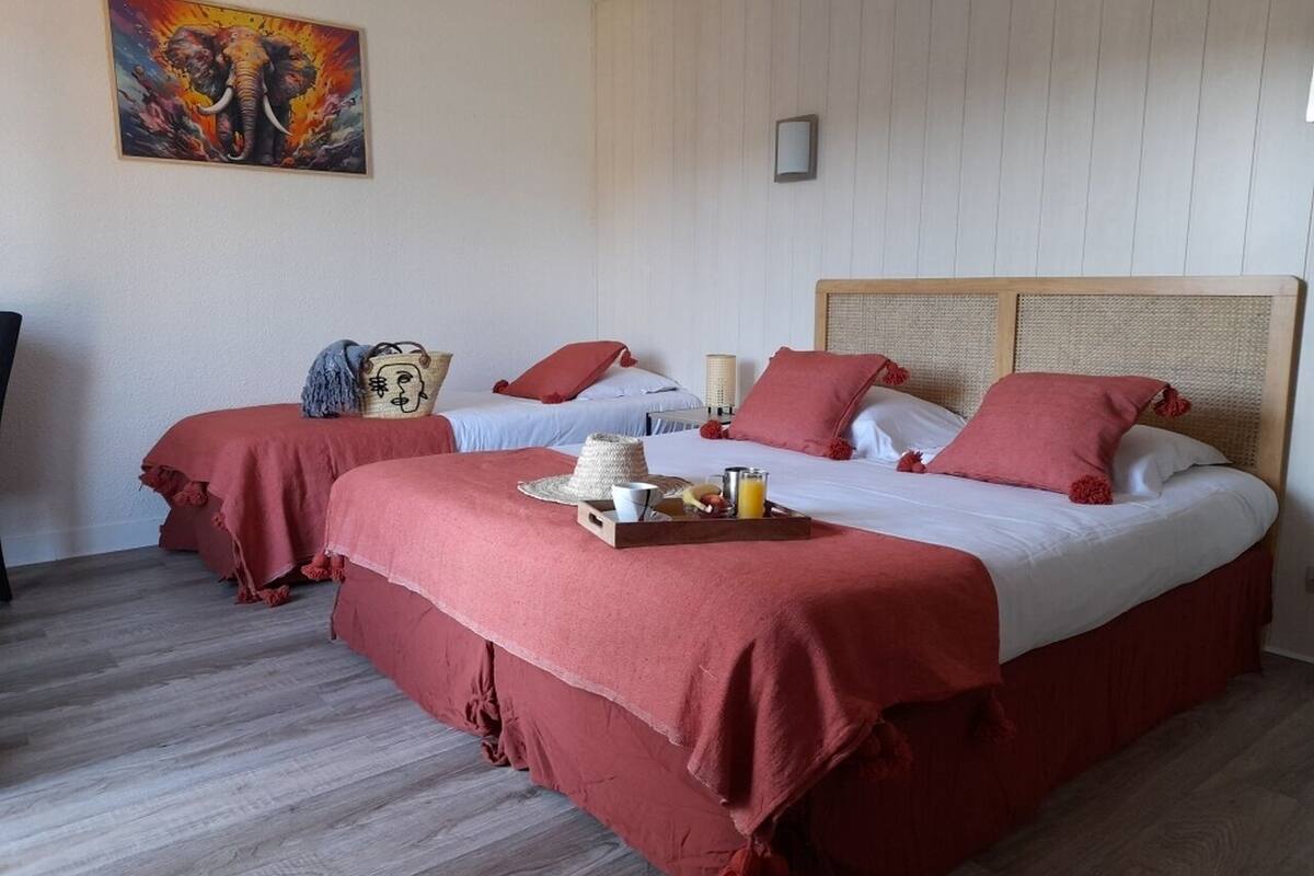A hotel room with two beds, red bedding, a tray with breakfast items, and a painting of an elephant on the wall.