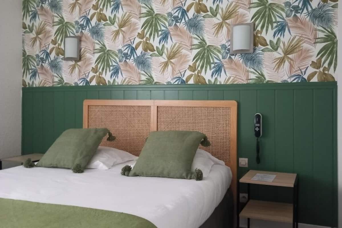 A hotel room with a bed, green walls, a rattan headboard, two green pillows, a bedside table with a lamp, and a telephone.