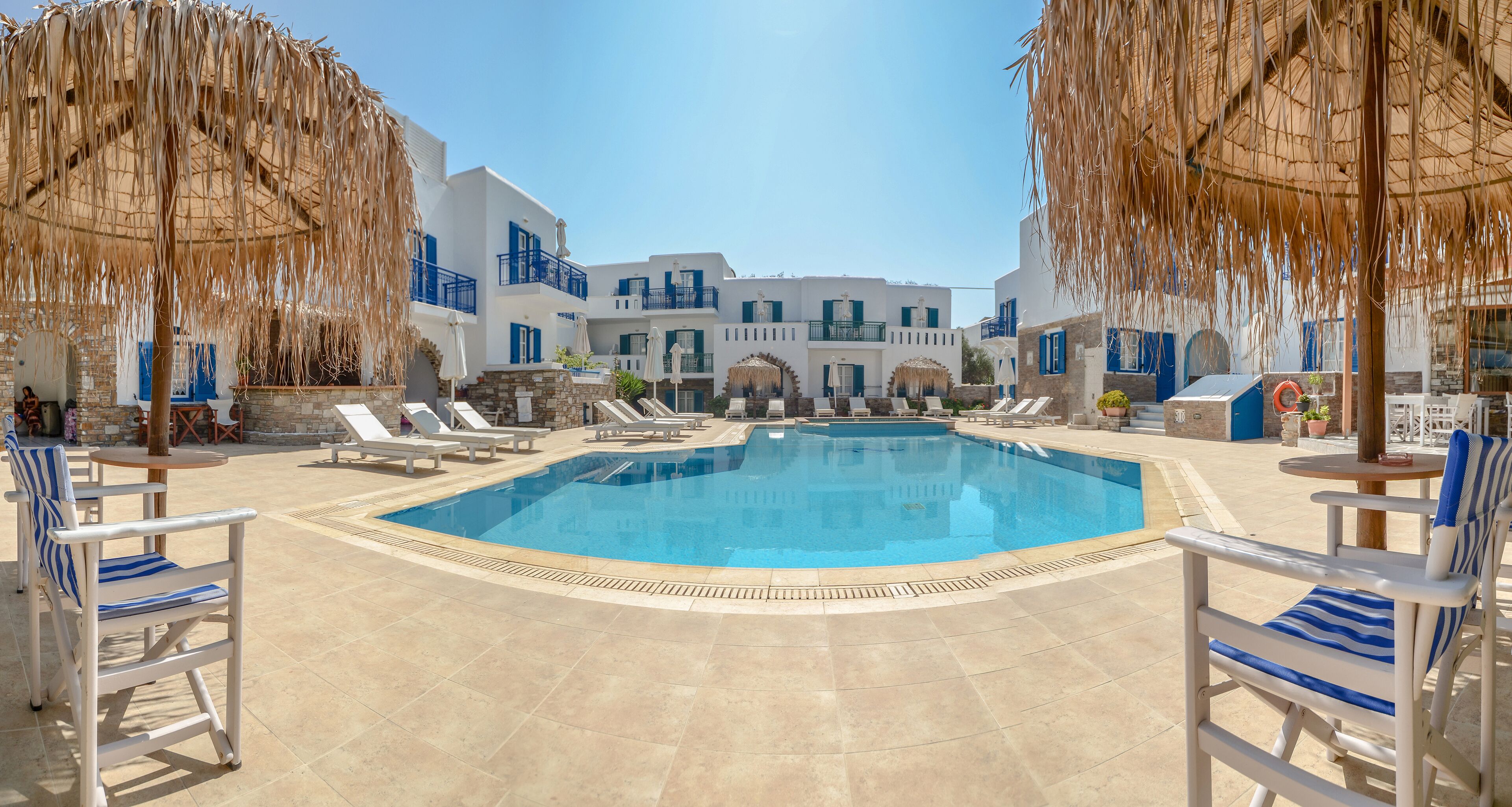 A swimming pool with lounge chairs and umbrellas, surrounded by white buildings with blue accents.