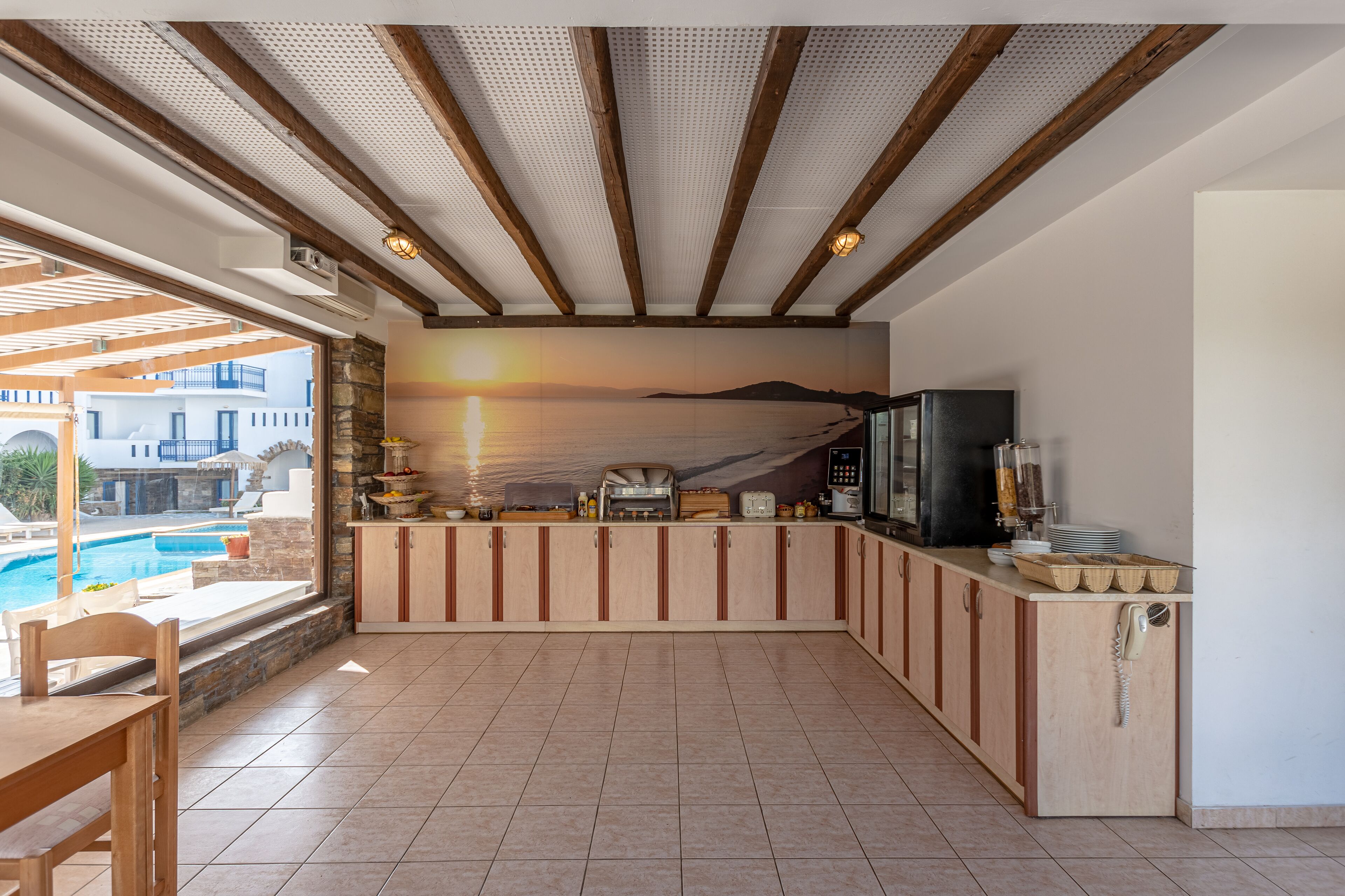 A kitchen with a view of a pool and sunset, wooden cabinets, and a phone on the counter.