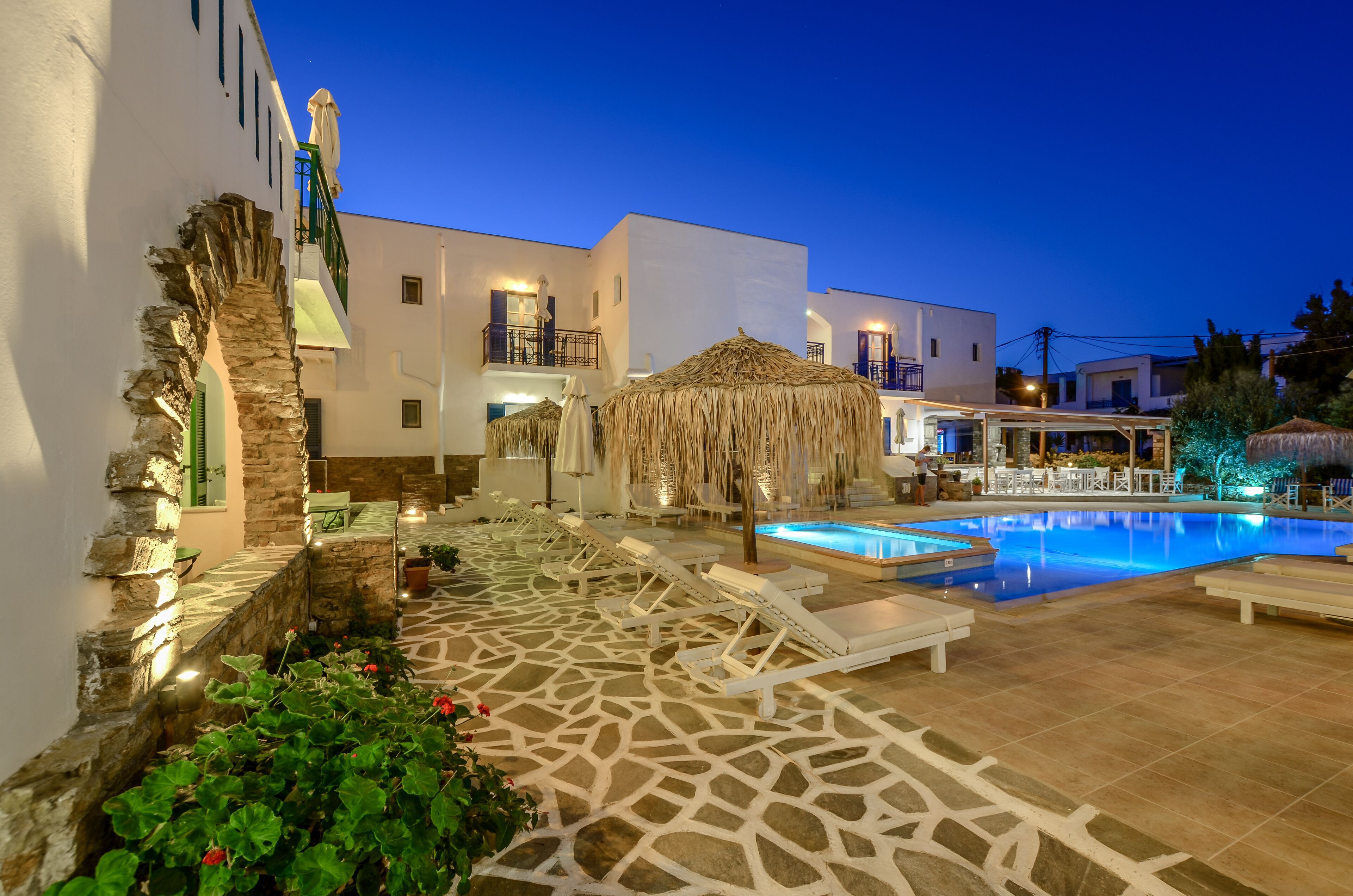 Un área de piscina con sillones de descanso, un muro de piedra y una sombrilla de paja.