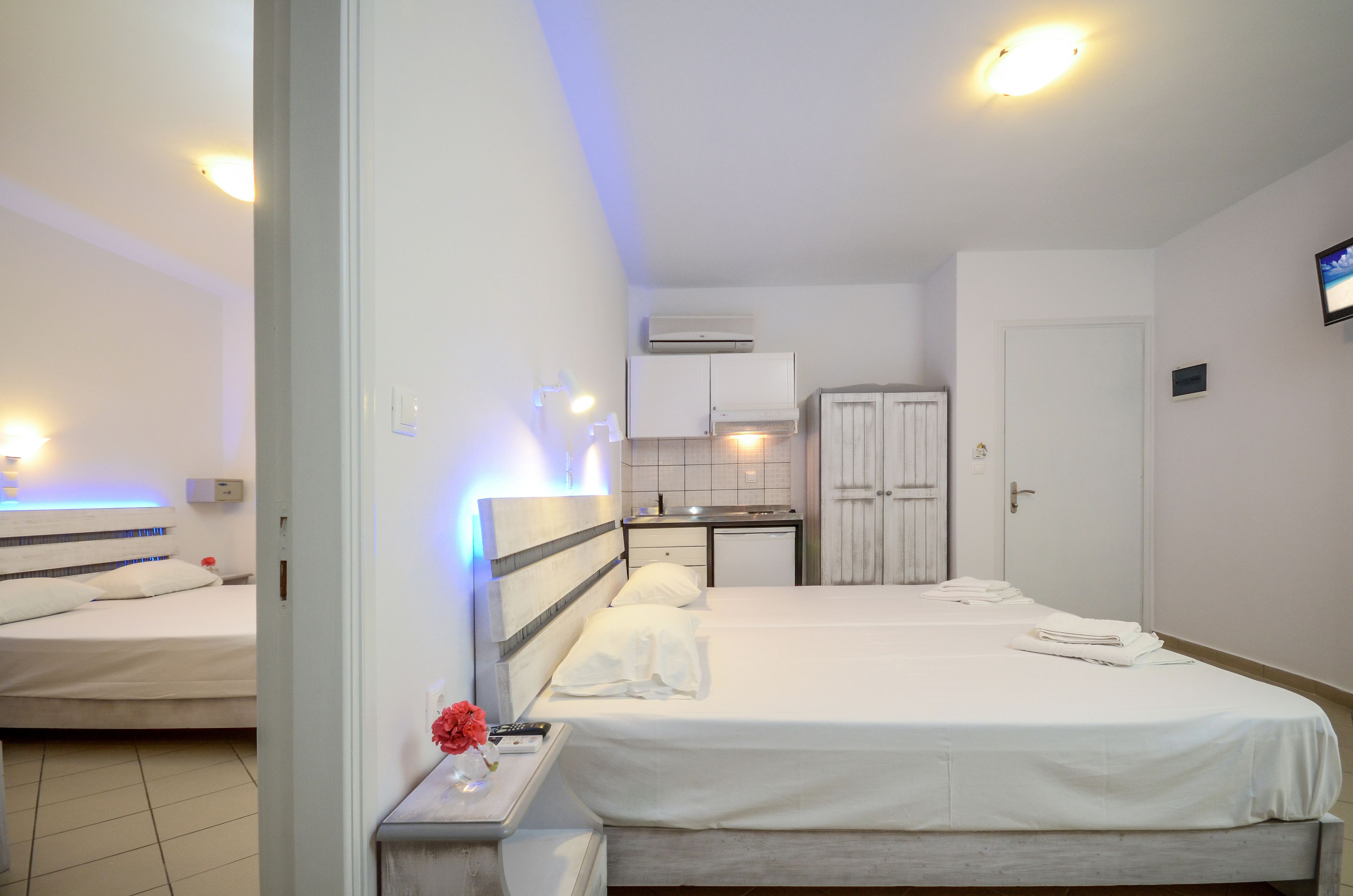 Habitación de hotel con dos camas, una kitchenette pequeña, un baño y un televisor en la pared.