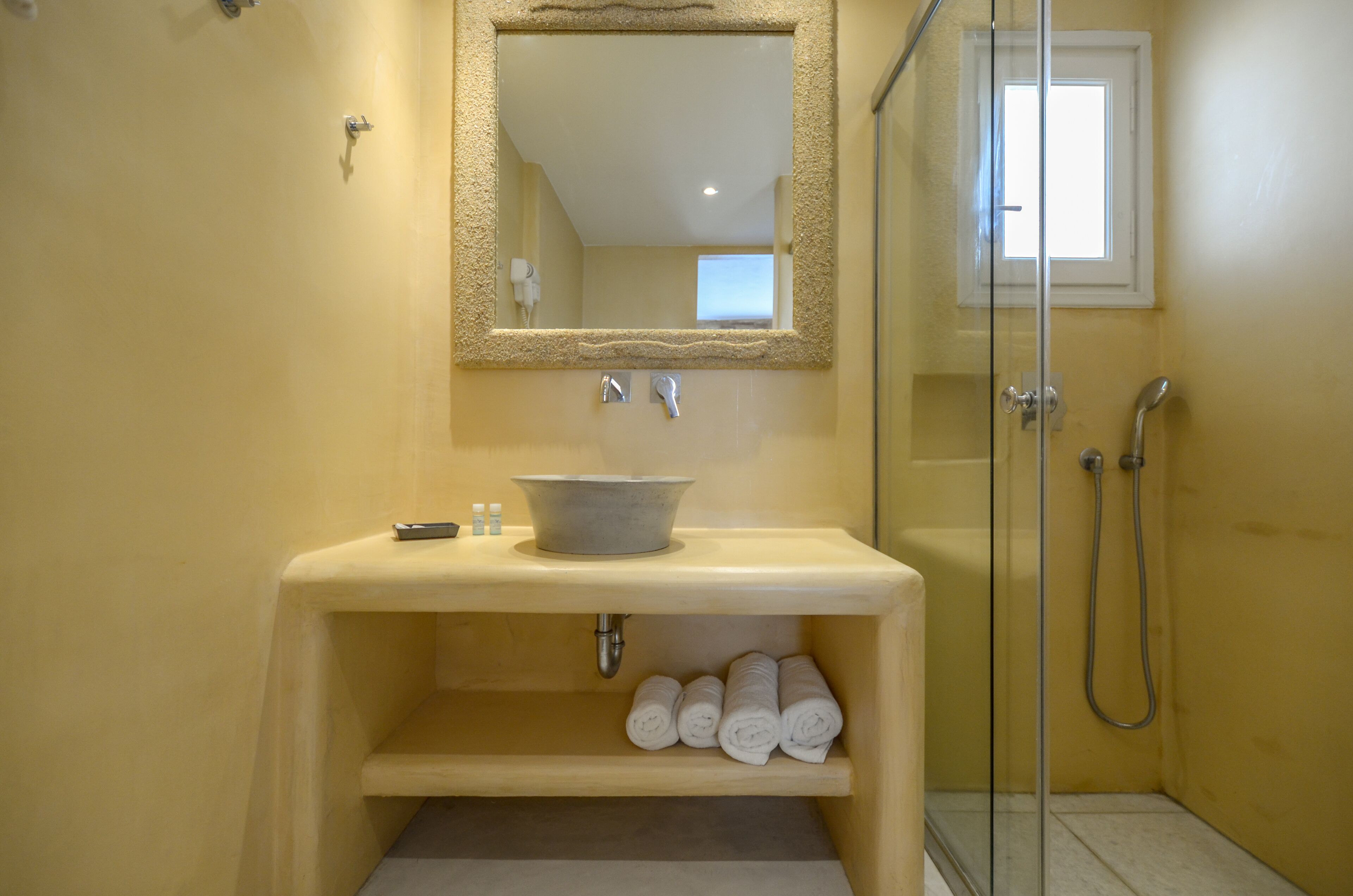 Un baño con un lavamanos color beige, un espejo, una ducha y una ventana.