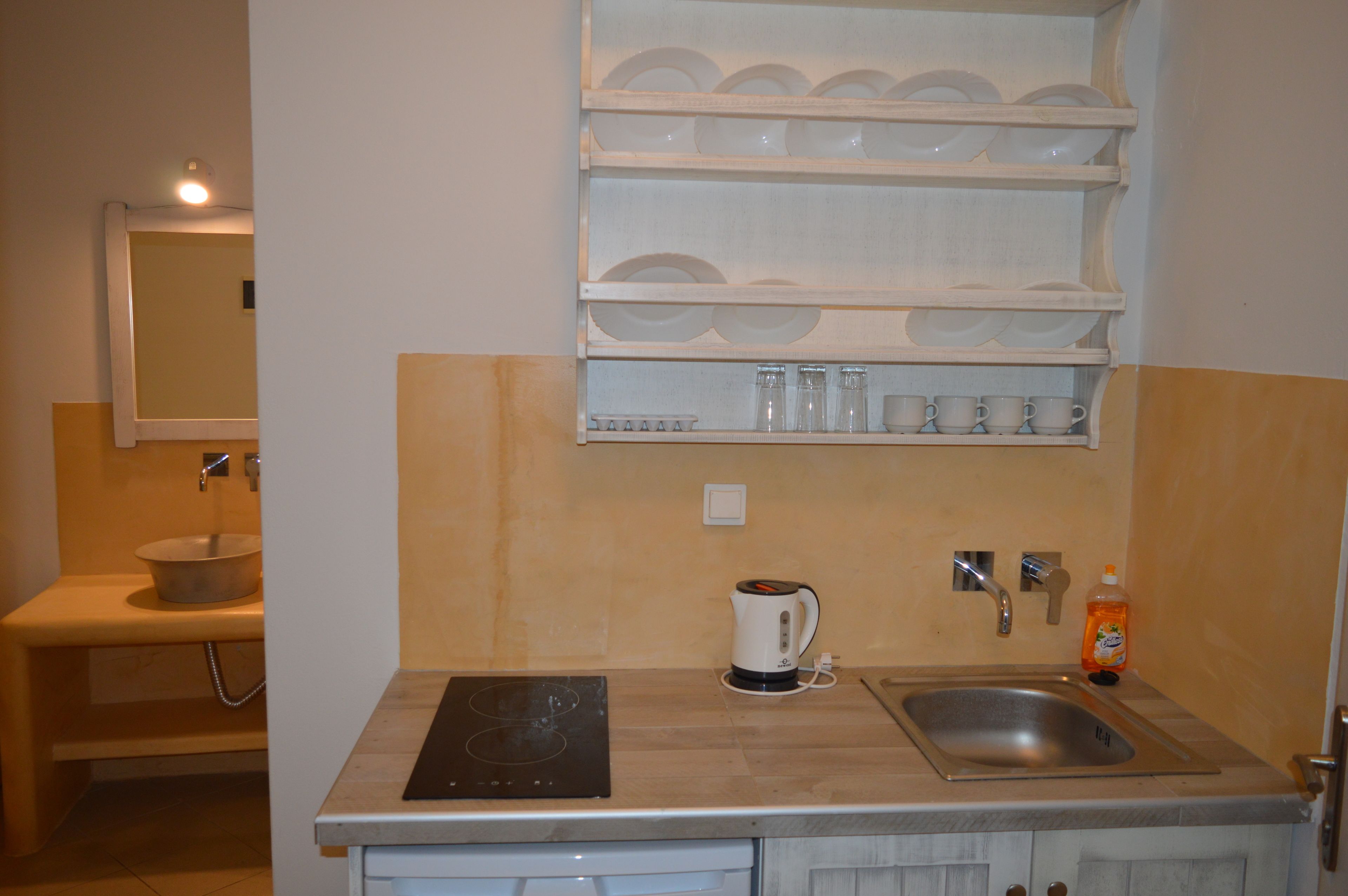 A compact kitchen with a sink, a kettle, and a dish rack.