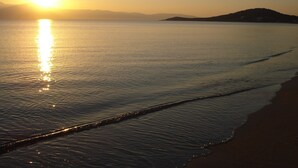 Una playa con aguas tranquilas que reflejan el sol, una orilla arenosa y colinas lejanas.