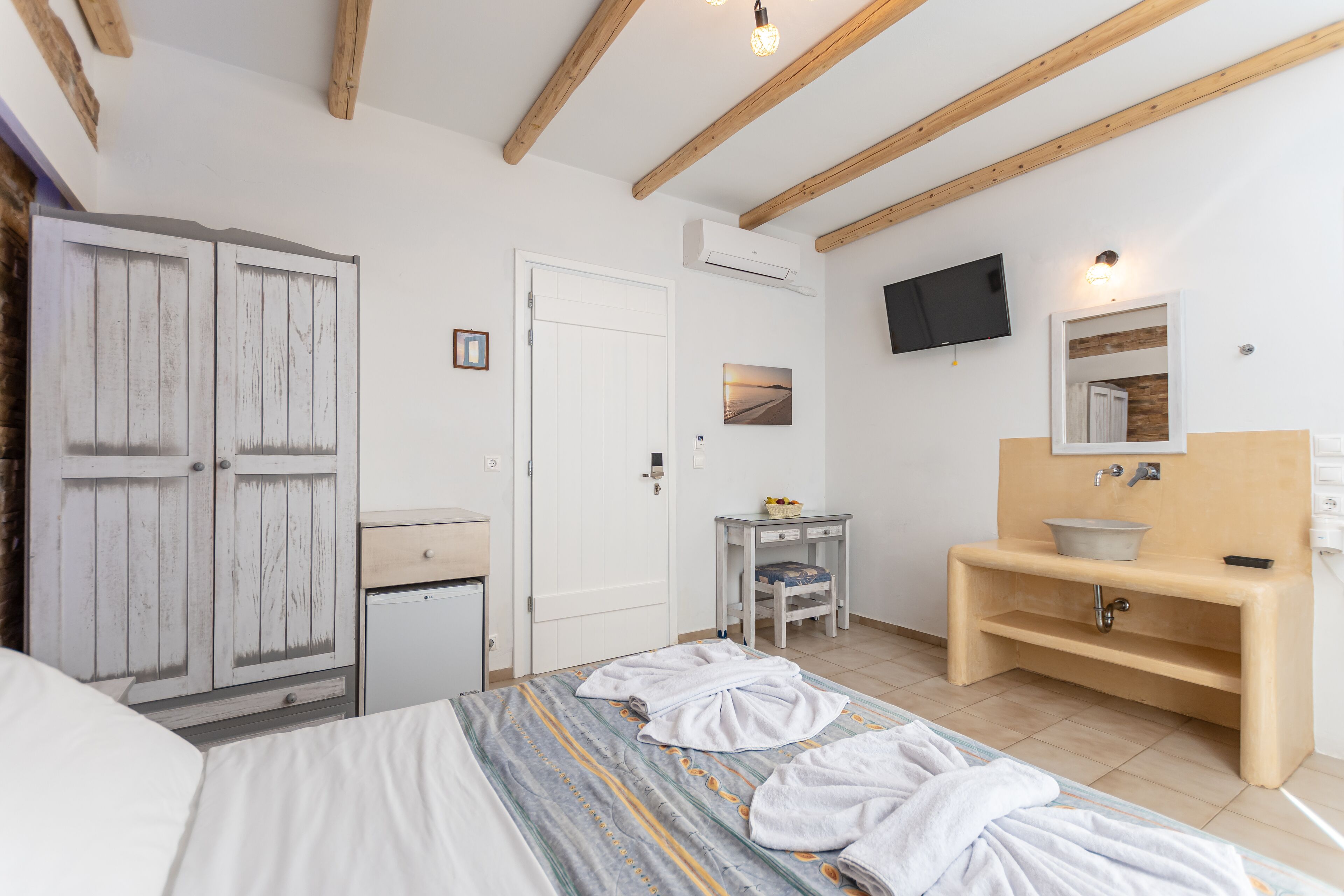 A bedroom with a bed, wardrobe, bedside table, and a bathroom with a sink and mirror.