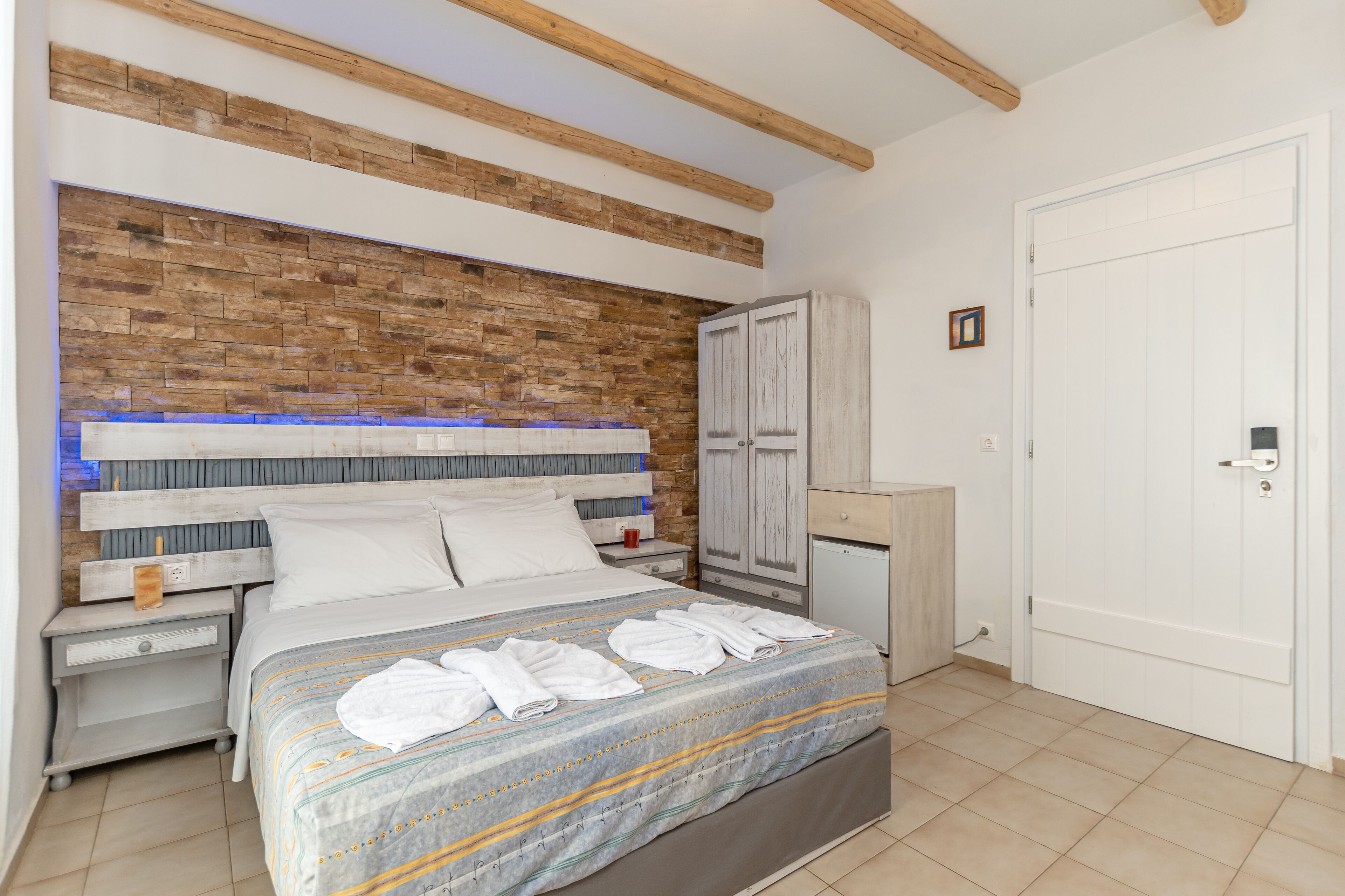 A bedroom with a brick-patterned headboard, a bed with white linens, a nightstand, a wardrobe, and a door.