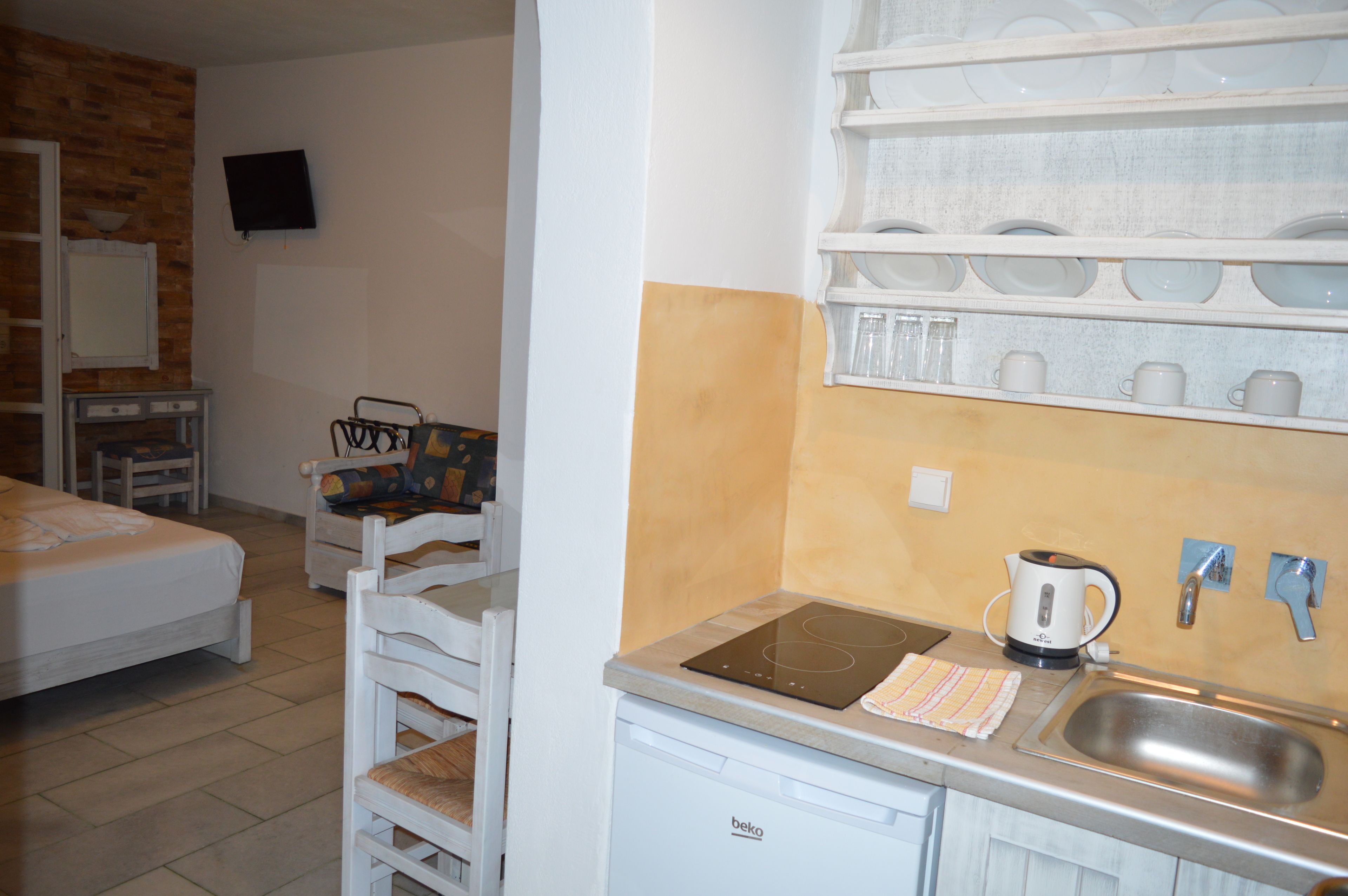 A compact hotel room with a kitchenette, a bed, a TV, and a dining area with chairs and a table.