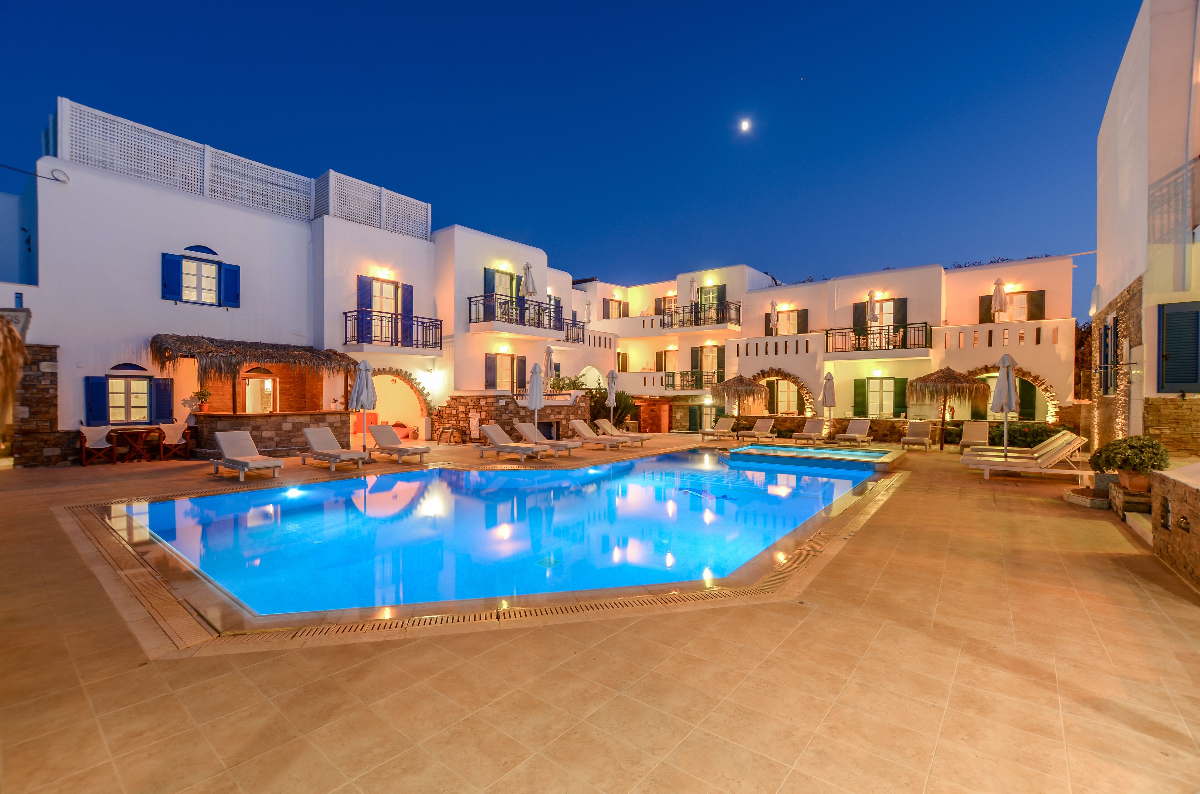 A swimming pool surrounded by white buildings with balconies, some with umbrellas.