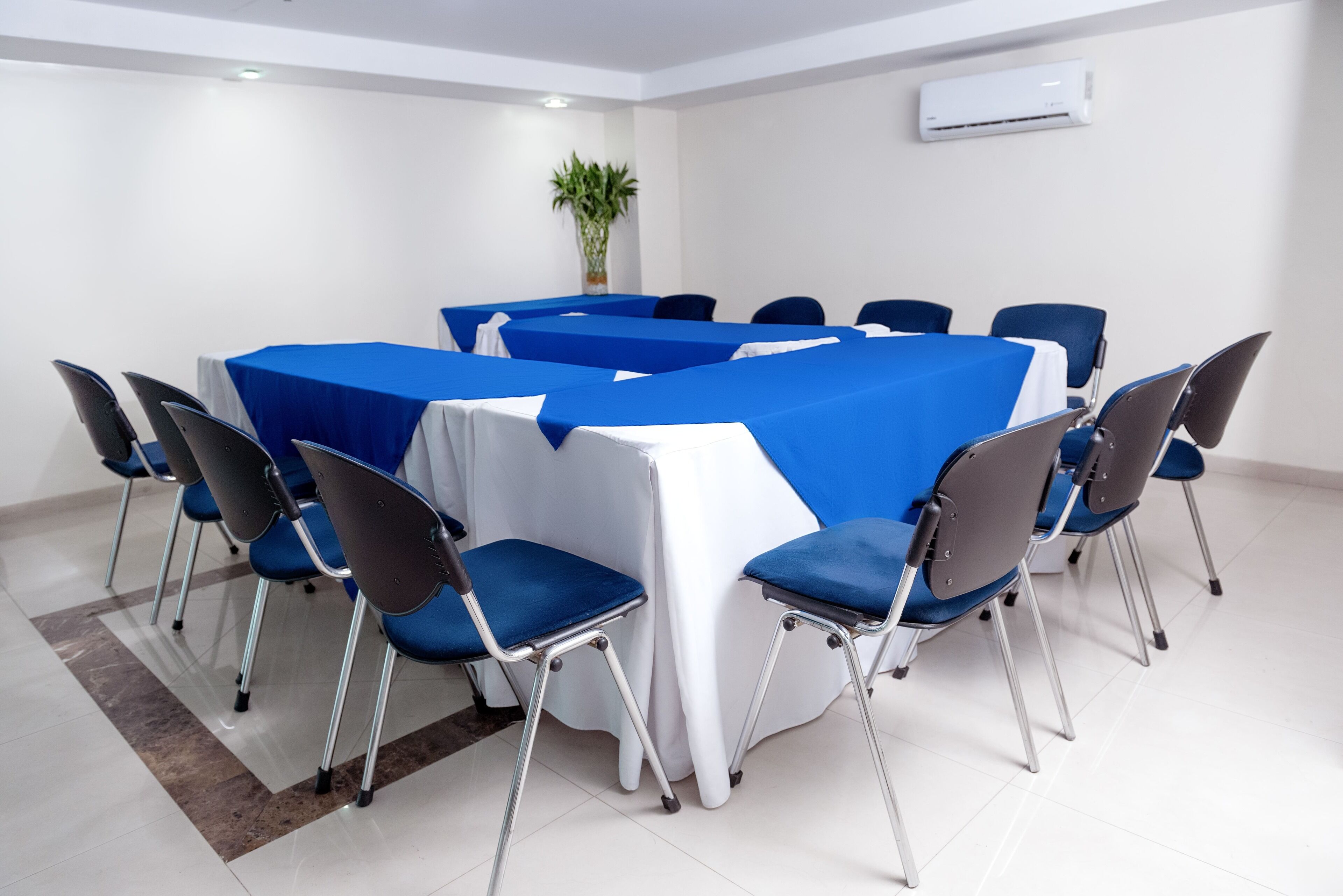 Une salle de conférence avec une grande table recouverte de nappes bleues et blanches, entourée de chaises bleues.