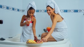 Two individuals in a bathtub with towels on their heads, holding drinks and a plate of food. - Hotel Plaza Las Americas Cali (Cali)