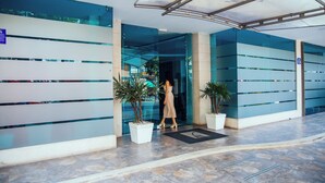 A modern building entrance with glass walls, potted plants, and a tiled floor. - Hotel Plaza Las Americas Cali (Cali)