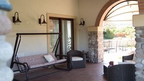 A covered patio area with a swing chair, wicker furniture, stone pillars, and a view through an archway. - Agriturismo Bacche di Bosco (Verona)