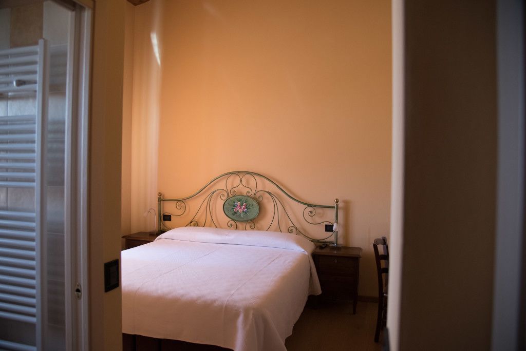 A bedroom with a single bed, a nightstand, a chair, and a door with blinds.