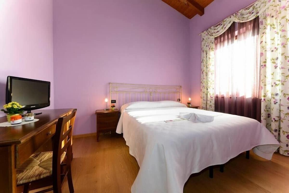 A bedroom with a bed, bedside tables, a desk, a chair, and a television.