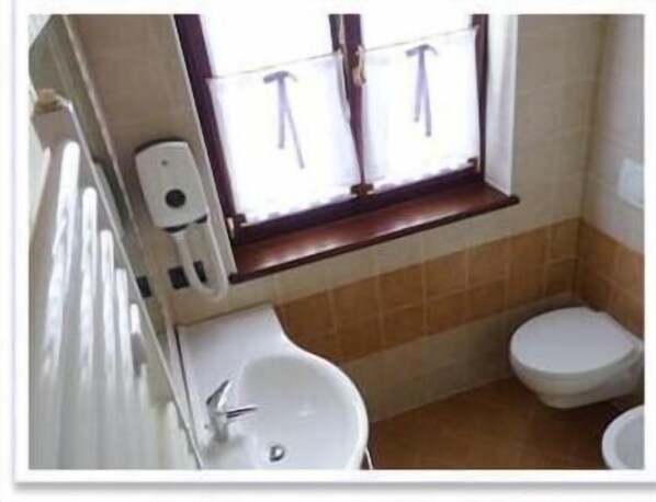 Baño con lavamanos, inodoro y ventana con persianas.
