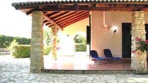 A covered outdoor seating area with stone pillars, two blue lounge chairs, and a stone-tiled floor. - Casa Vacanza Ondablu (Ispica)