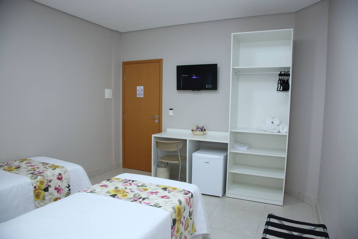 Ein Hotelzimmer mit zwei Betten, einem Schreibtisch, einem Fernseher und einem Kleiderschrank.