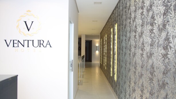 A hallway with a wall-mounted sign for Ventura Hotel, a patterned wall, and a corridor leading to another room. - Ventura Hotel (Barreiras)
