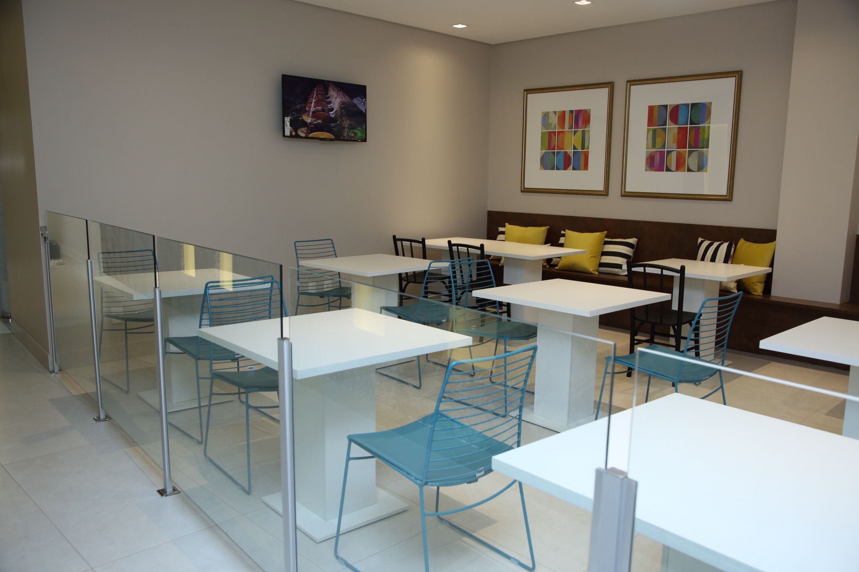 A modern dining area with glass partitions, white tables, and blue chairs.