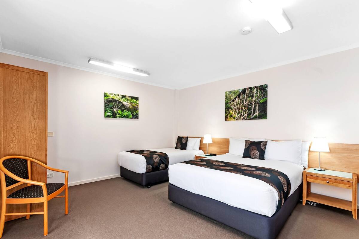 A hotel room with two beds, a wooden chair, a nightstand, and two wall-mounted pictures.