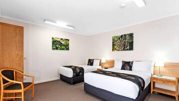 A hotel room with two beds, a wooden chair, a nightstand, and two wall-mounted pictures.