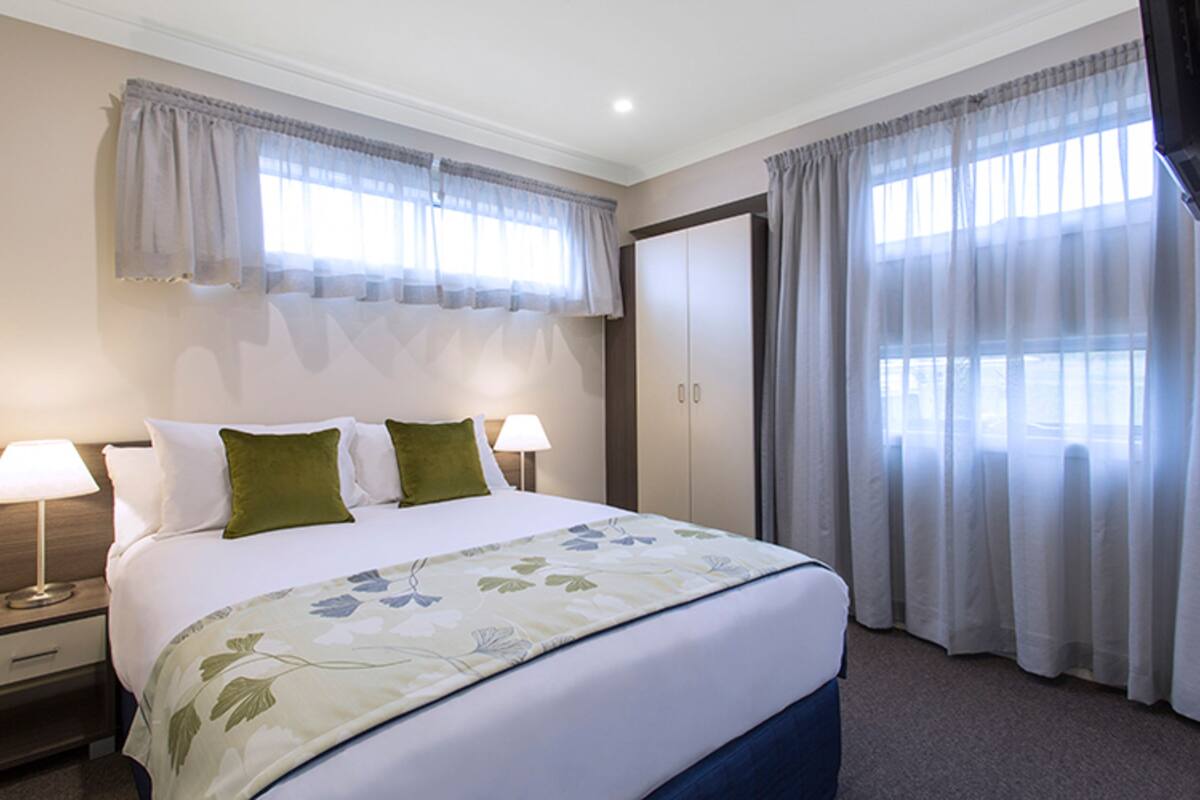 A hotel room with a large bed, two bedside lamps, a nightstand, a wardrobe, and a window with curtains.