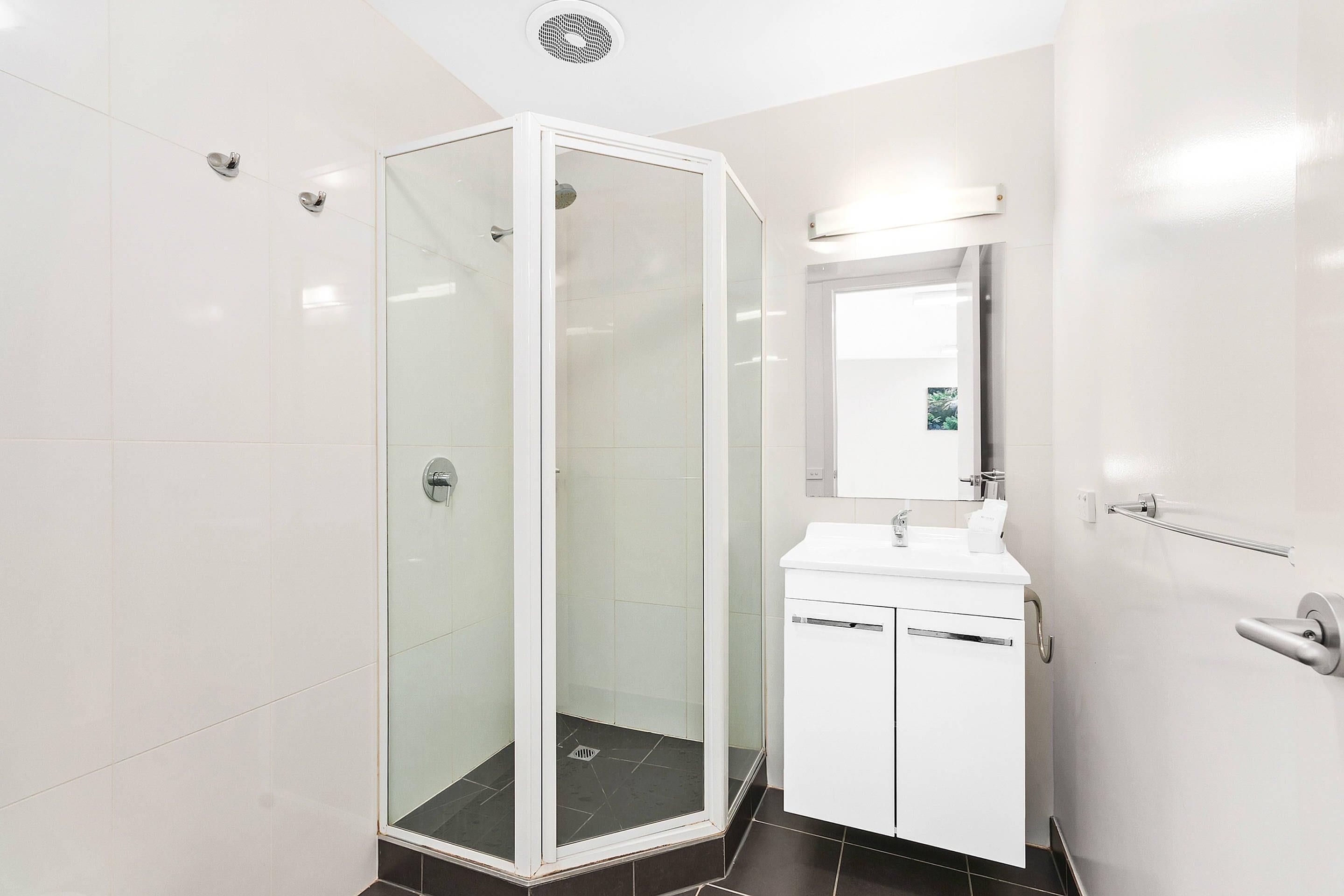 Une salle de bain moderne avec une douche à parois de verre, un lavabo blanc et un miroir au-dessus.
